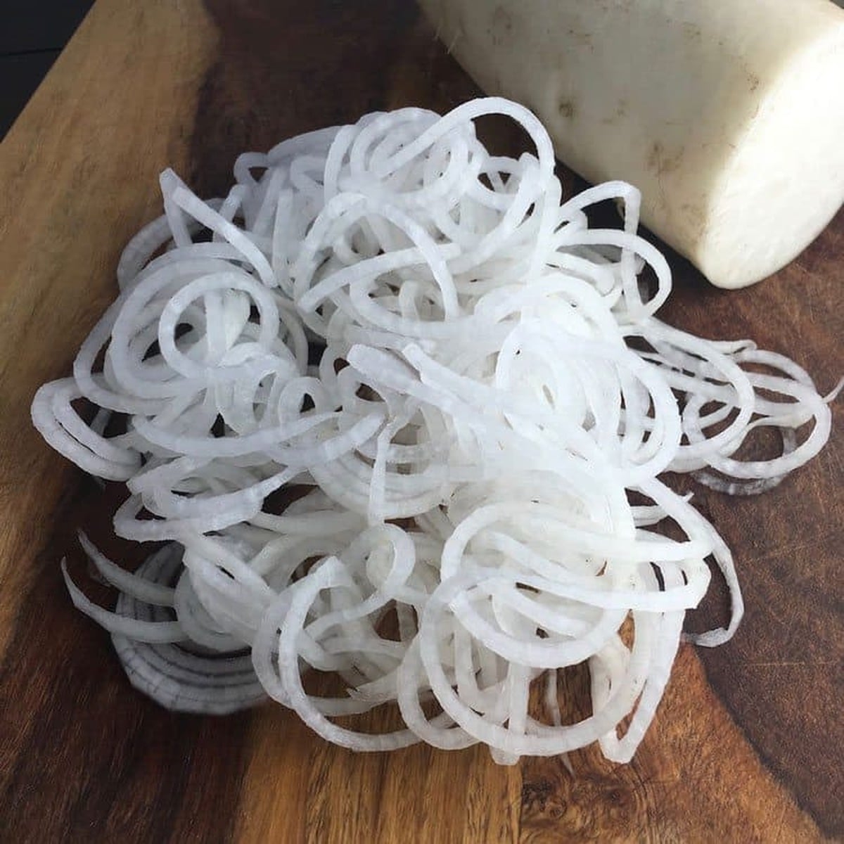 Spiralized daikon noodles piled on a wooden board next to a whole white daikon radish