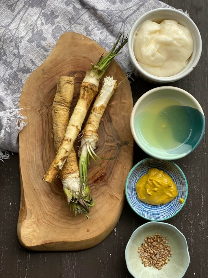 Fresh horseradish roots on a wooden board with small bowls of sauce ingredients
