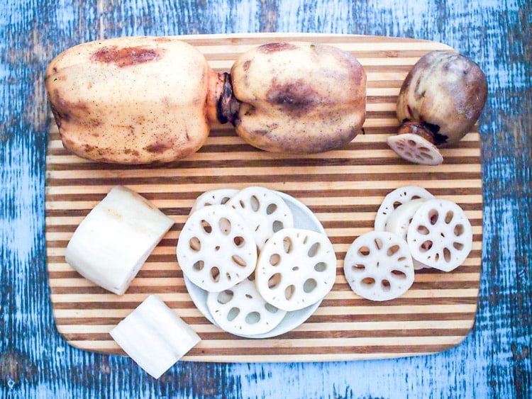 Whole lotus roots and lacy lotus root slices on a striped cutting board