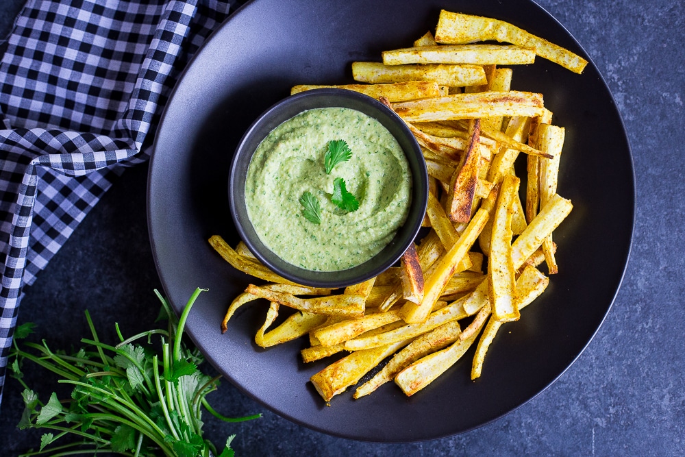 Curried parsnip fries on a dark plate with a green cilantro hummus dip