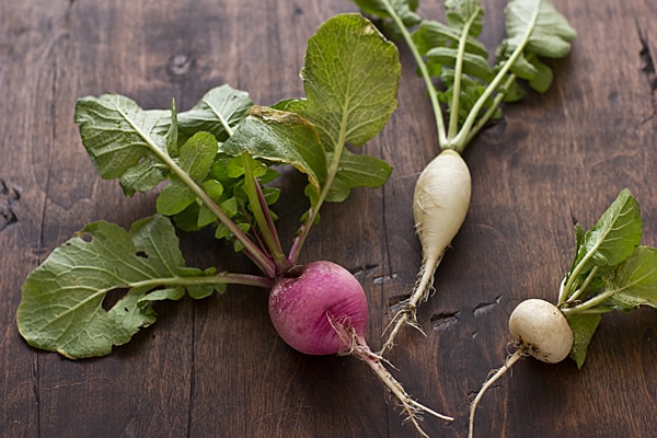Freshly harvested white radishes and a pink radish with their green leaves on a wooden table