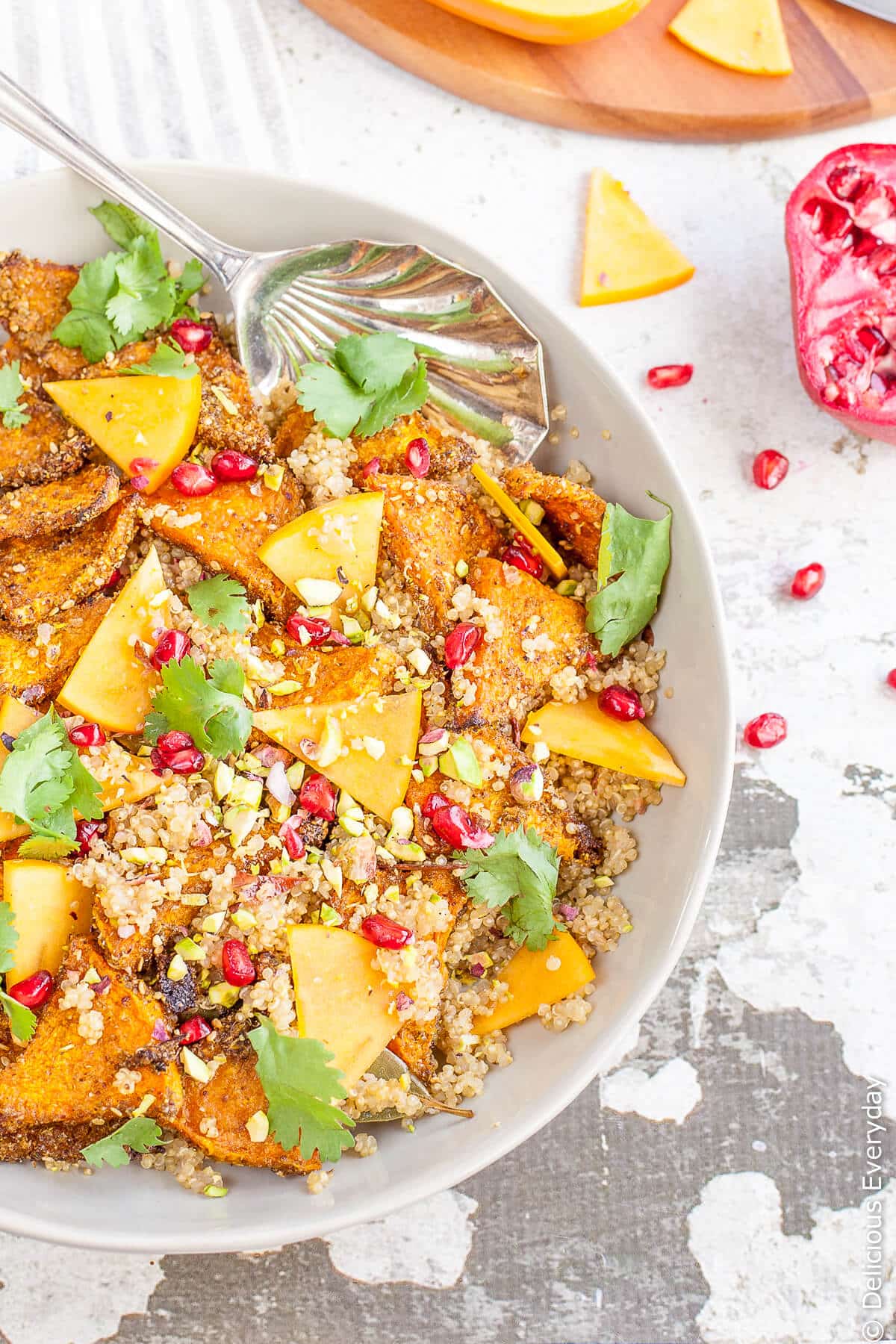 Za'atar pumpkin quinoa pilaf topped with persimmon, pomegranate seeds, pistachios and cilantro in a white bowl