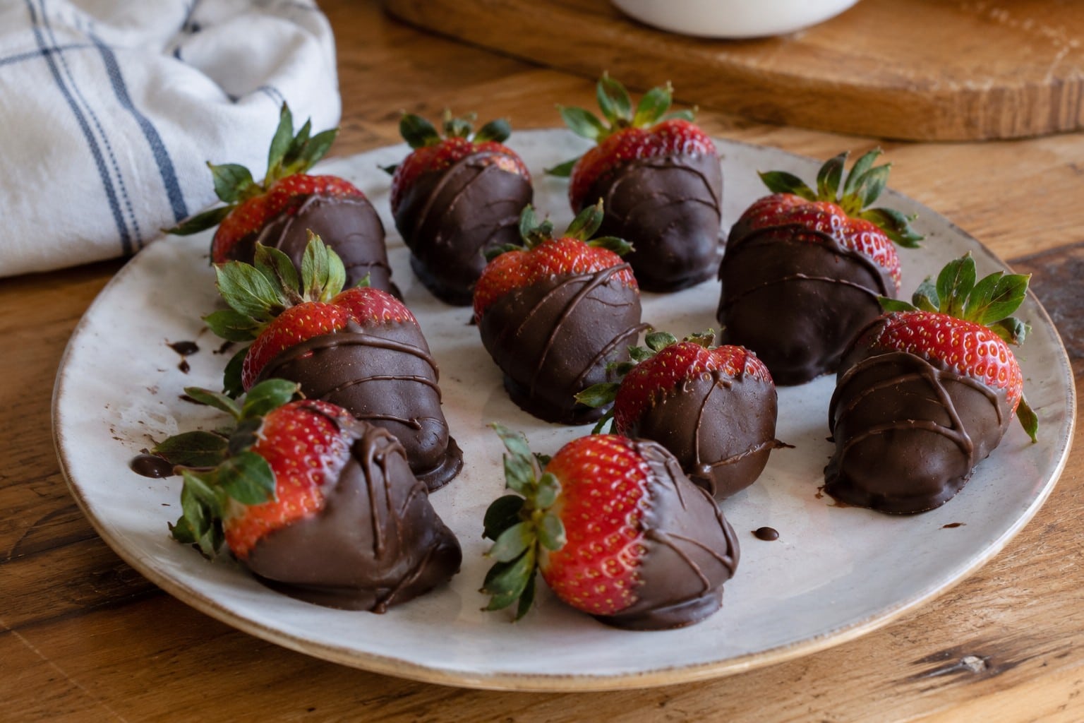 Dairy-free chocolate dipped strawberries arranged on a rustic plate on a wooden table