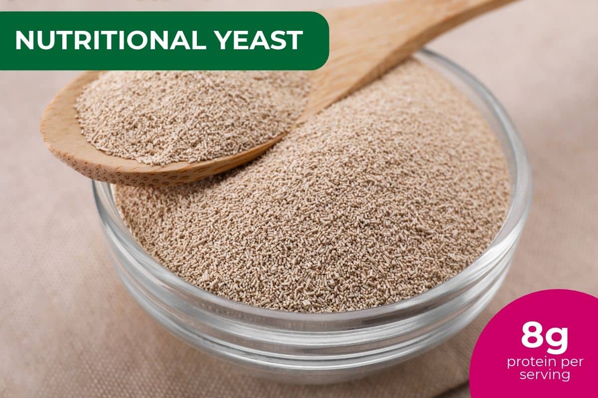 Glass bowl of nutritional yeast with a wooden spoon, labeled 8 g protein per serving