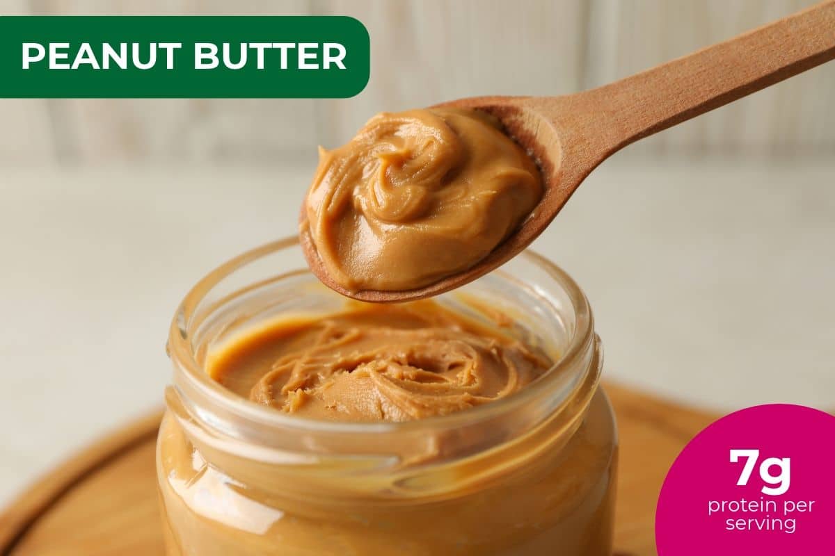 Spoonful of creamy peanut butter over an open jar, labeled 7 g protein per serving