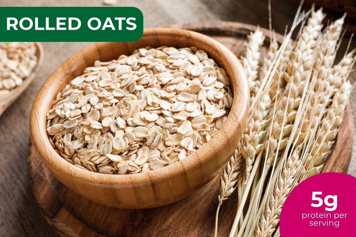 Wooden bowl of rolled oats beside wheat stalks, labeled 5 g protein per serving