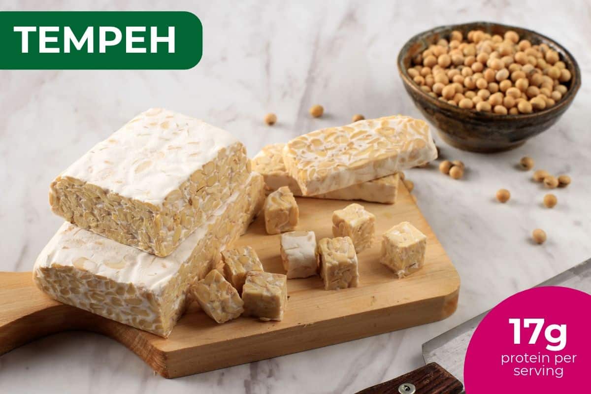 Blocks and cubes of tempeh on a cutting board with soybeans, labeled 17 g protein per serving