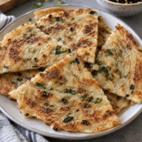 Crispy, flaky vegan scallion pancakes cut into wedges on a white plate
