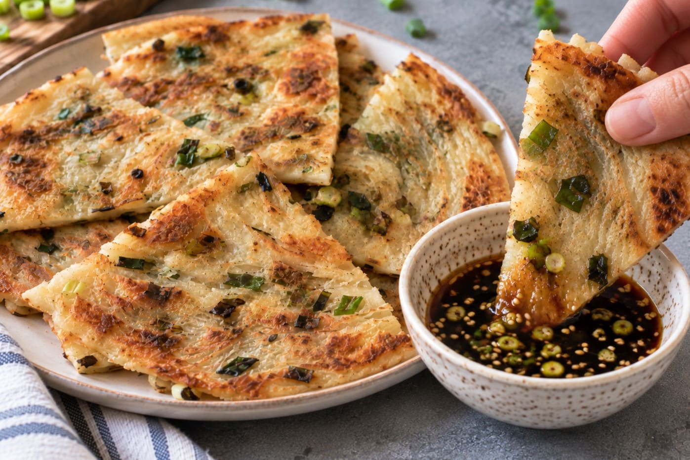 Scallion pancake wedge being dipped into a speckled bowl of soy sesame dipping sauce